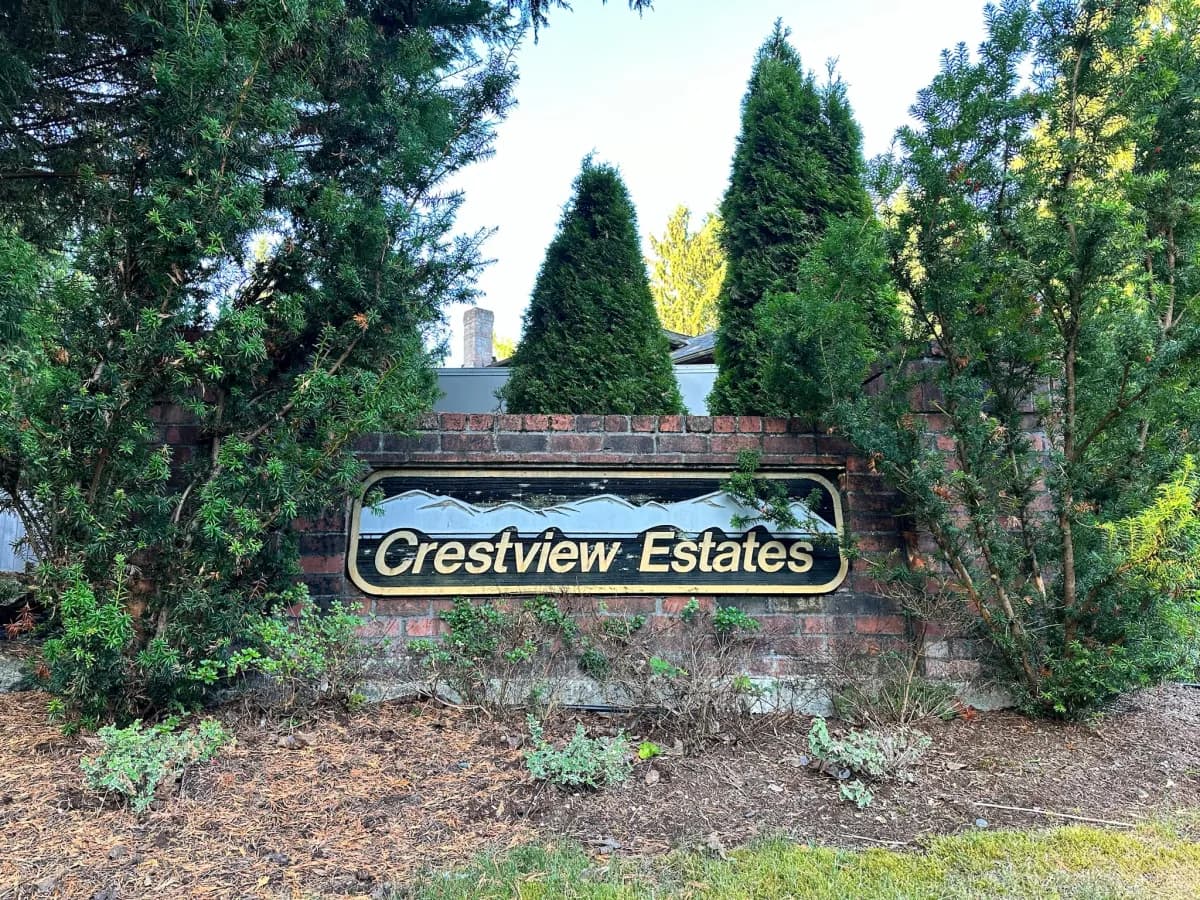 Crestview Estates brick entry sign with gold mountain motif flanked by columnar cedars in Duvall WA